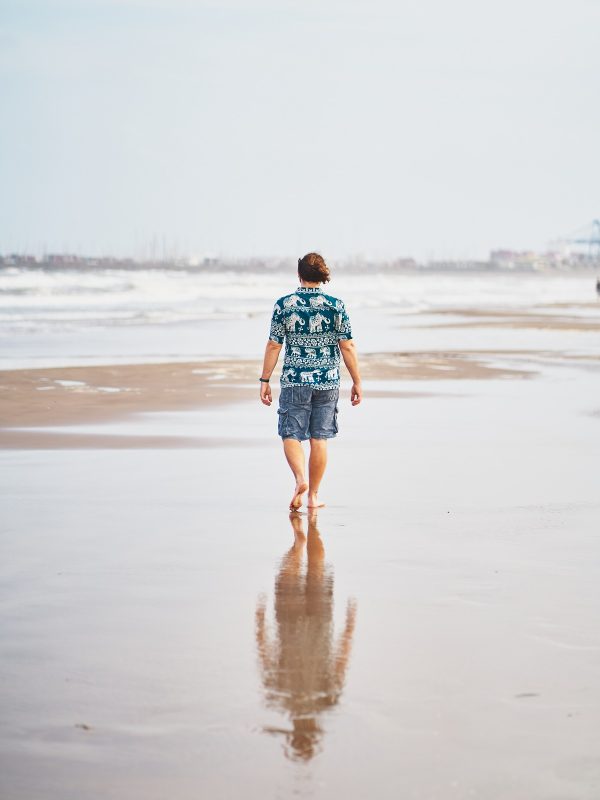Back view of barefoot male in summer outfit walking on wet sandy Malvarrosa beach in Valencia