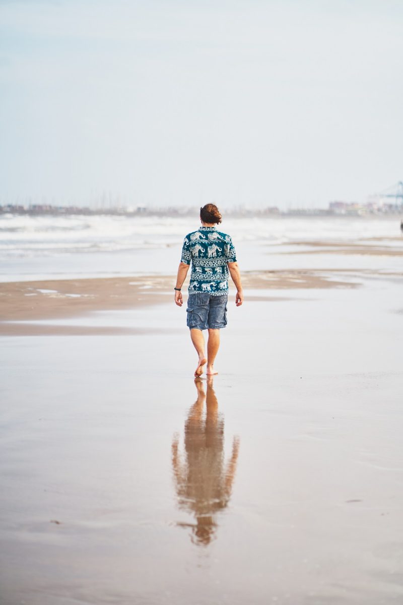 Back view of barefoot male in summer outfit walking on wet sandy Malvarrosa beach in Valencia
